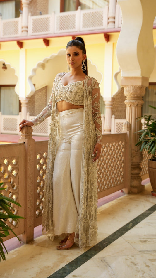 Woman in traditional outfit standing on a balcony with decorative columns and plants.