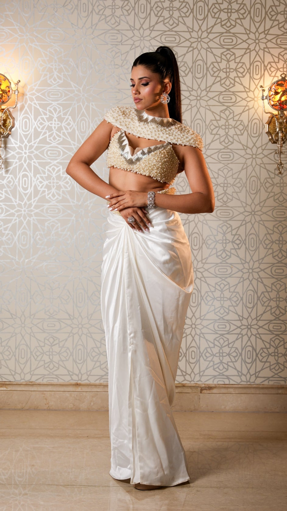 Woman in a white saree with gold blouse against a decorative wall.