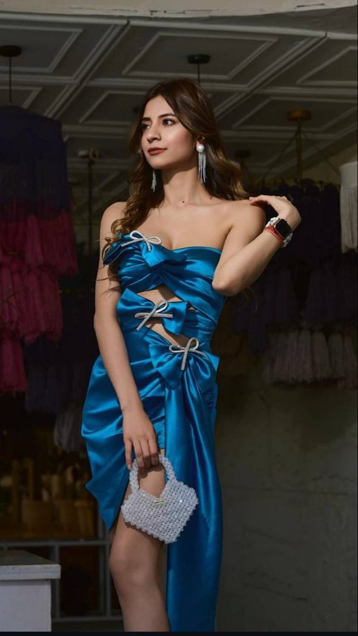 Woman in a blue dress holding a silver handbag in an indoor setting