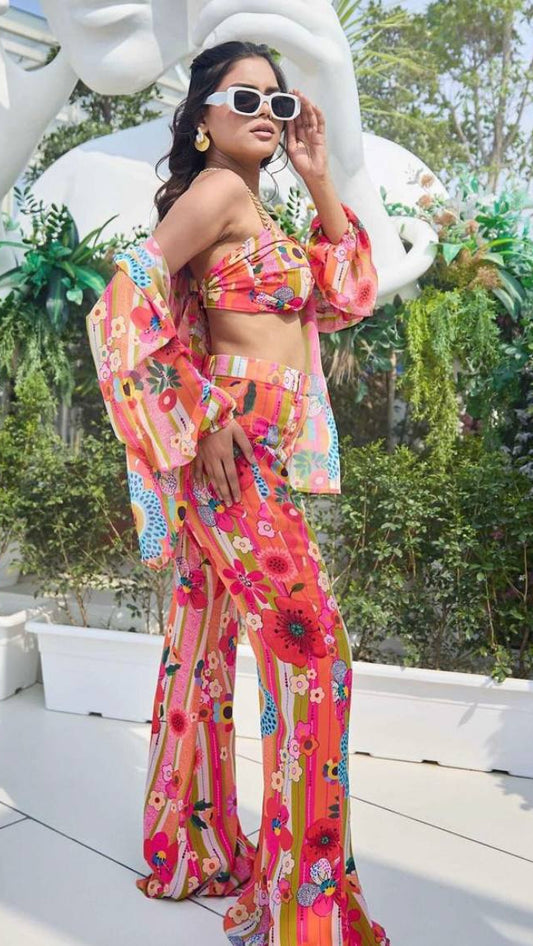 Woman in a colorful floral outfit standing outdoors with greenery and a sculpture in the background