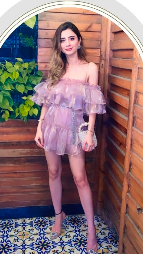Woman in a purple dress standing in a wooden outdoor setting with plants.