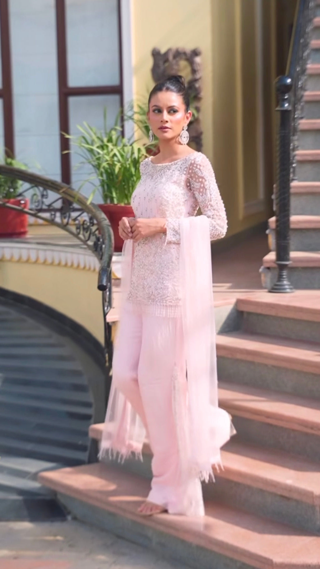 Woman in a light pink traditional outfit standing on steps outdoors.