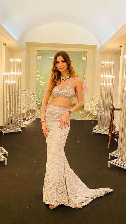 Woman in a silver dress standing in an elegant interior setting with decorative lights.