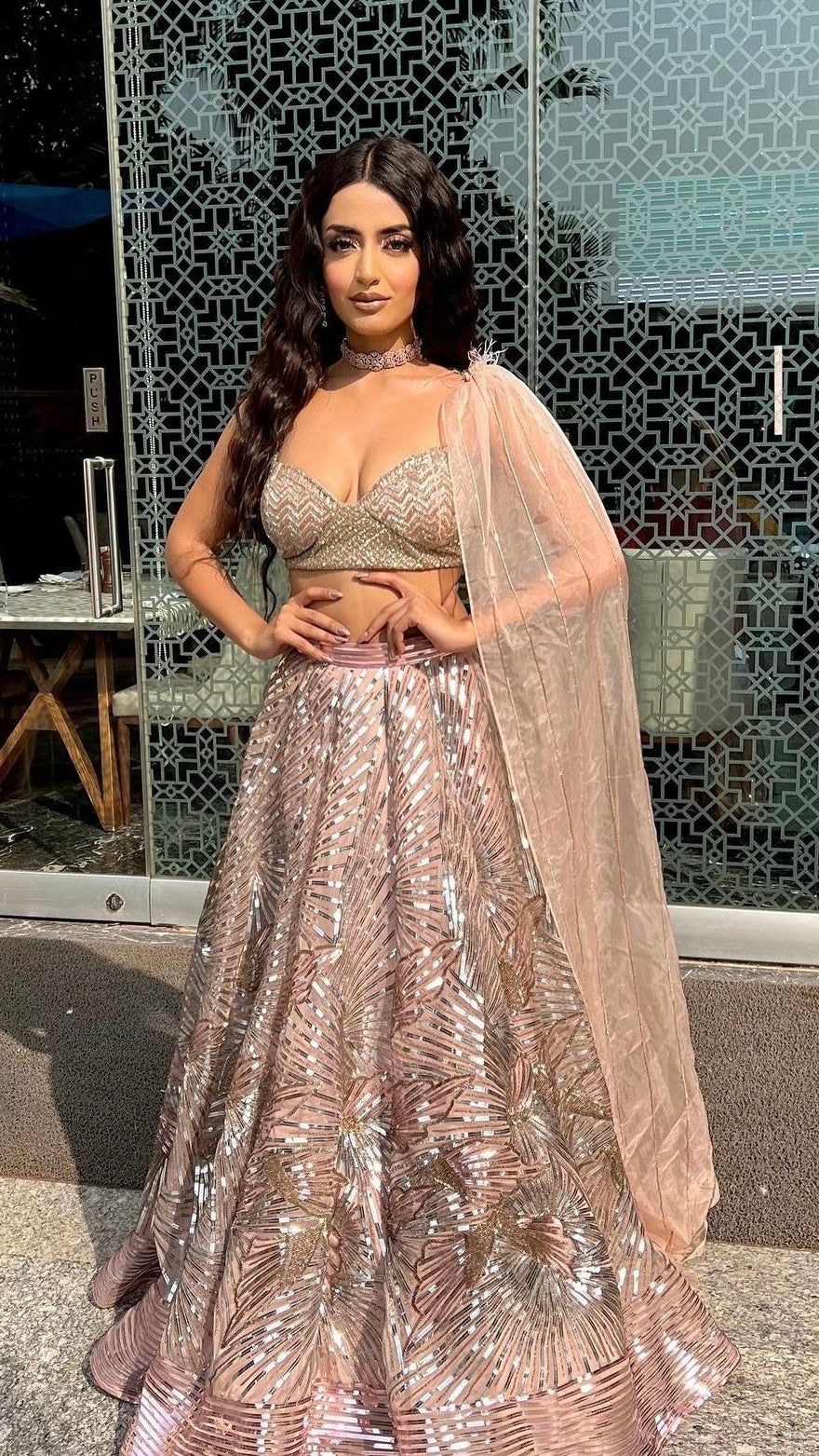 Woman in a sparkling outfit standing outdoors with a decorative wall in the background