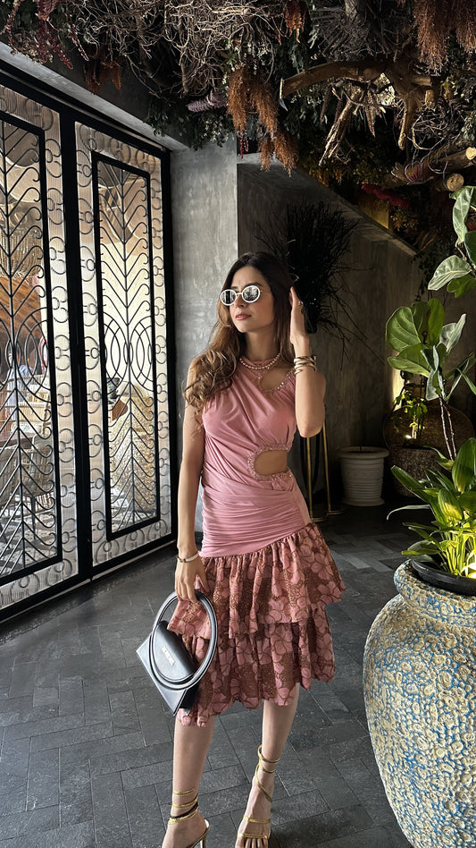 Woman in a pink dress standing in an indoor setting with plants and decorative elements.