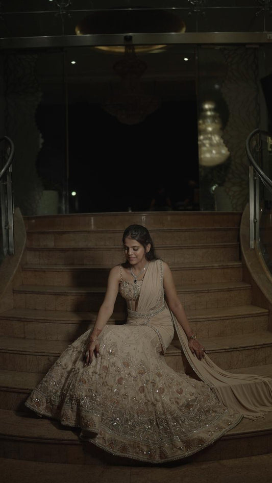 Woman in a beige evening gown sitting on a staircase in a dimly lit room.