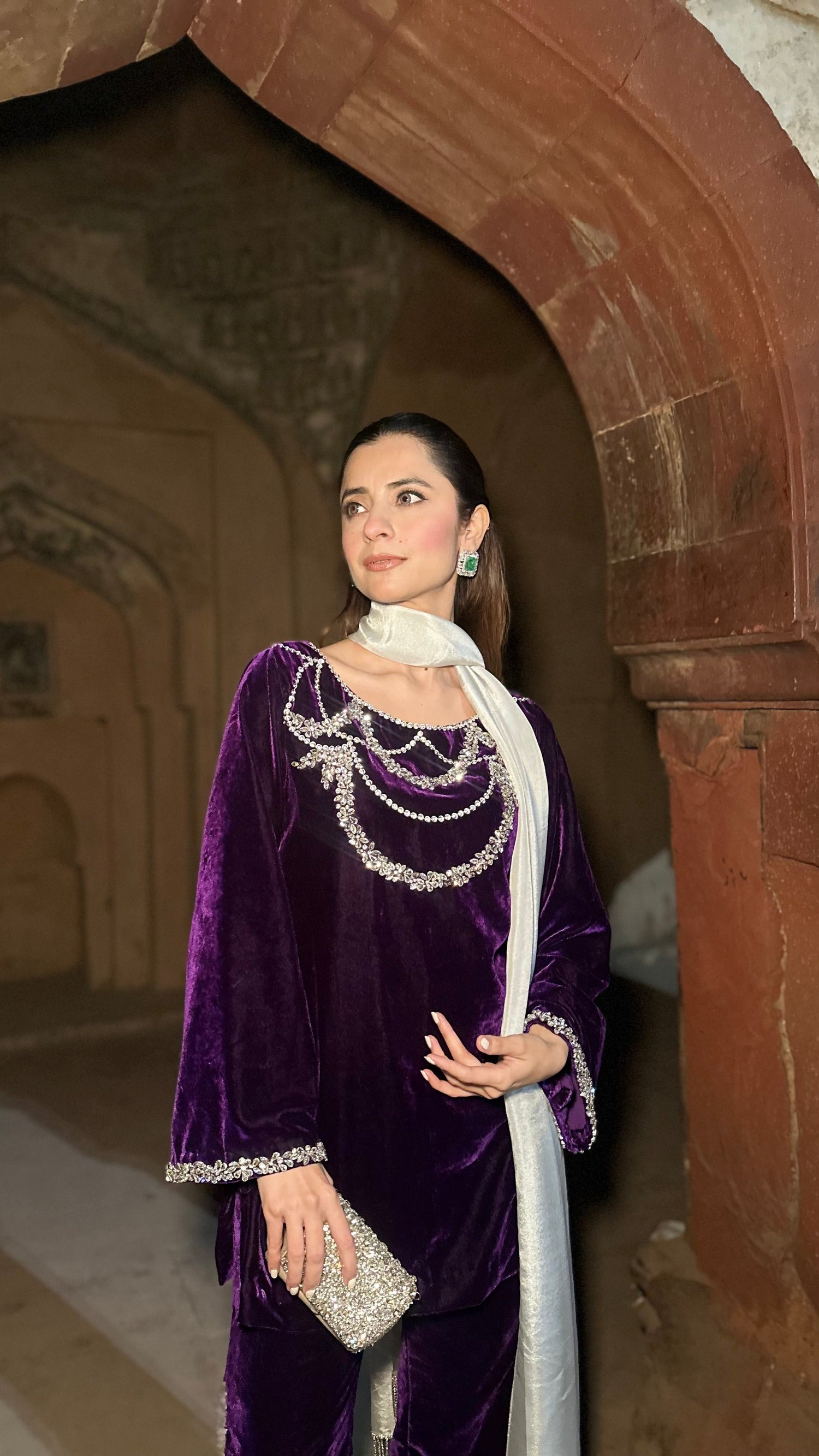 Woman in a purple traditional outfit standing in an archway with stone walls.