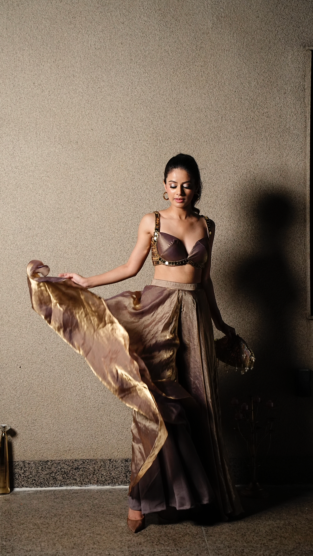 Woman in a flowing dress holding a large fabric against a plain wall.